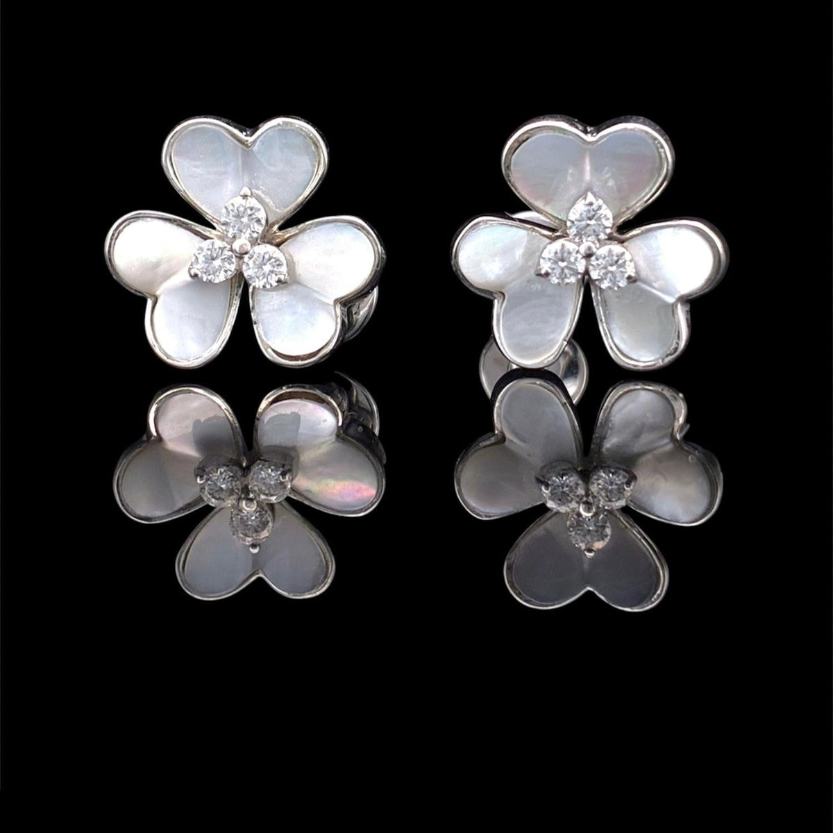 Impimo mother of pearl and moissanite flower stud earrings, 925 sterling silver with 18K white gold plating - the pair shown together in three-quarter view, hand-carved cream shell petals around a round moissanite centre.
