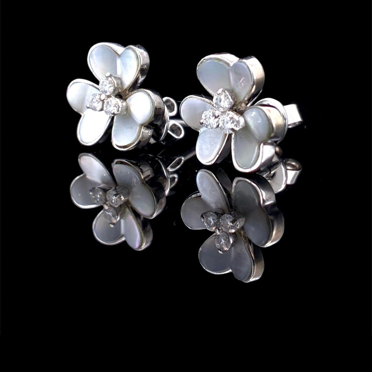 Impimo mother of pearl and moissanite flower stud earrings - the pair shown front on, four-petal shell flowers with moissanite centres on white metal.