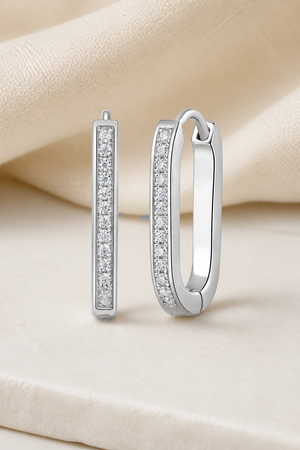 Impimo 0.15 CT (Total) Moissanite Round Cut Earrings - Elongated Pavé Huggie Hoop - 925 Sterling Silver with 18K White Gold Plating | display view on ivory linen