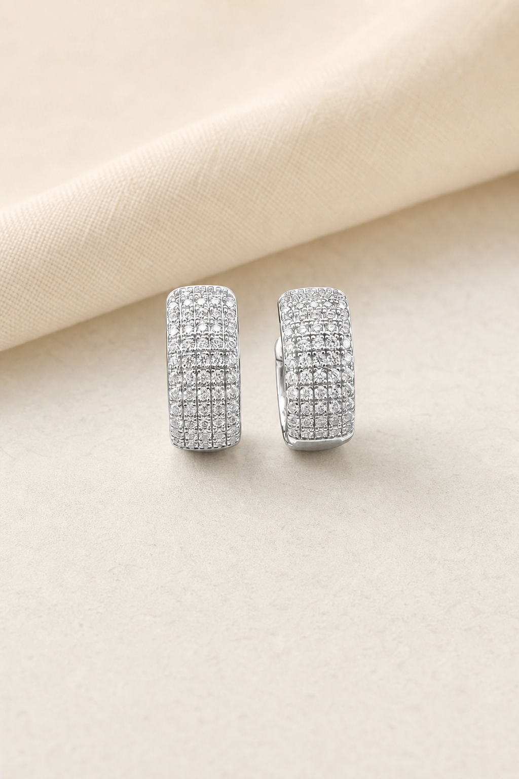 Impimo 0.6 CT (Pair) Moissanite Round Cut Earrings - Pavé Cylinder Huggie Hoop - 925 Sterling Silver with 18K White Gold Plating | display view on ivory linen