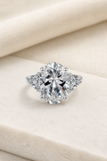 Impimo 8 CT Moissanite Oval Cut Ring - Three-Stone with 0.50 CT Trillion Sides - 925 Sterling Silver with 18K White Gold Plating | display view on ivory linen